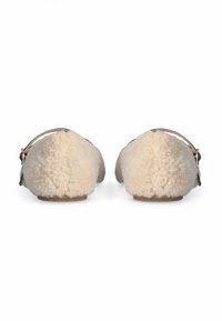 Een paar beige slip-on schoenen bedekt met schapenvacht, met enkelbanden en gespen, gezien vanaf de achterkant op een witte achtergrond.