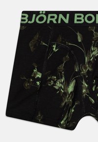 Bóxer negro con un patrón floral verde, con una cinturilla elástica verde y detalles de costura en contraste.