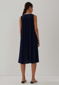 Navyblaues ärmelloses Kleid mit einem lockeren, fließenden Design; es hat kleine blaue und weiße Punkte und eine Länge bis zur Mitte des Waden. Verstellbare Träger.