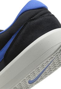 Talons de baskets noirs et bleus avec textures en daim et mesh, semelle en caoutchouc blanche arborant un logo Nike swoosh bleu sur la bande de roulement.