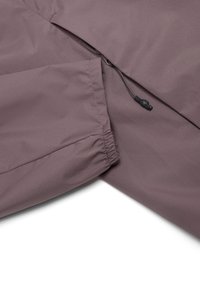 Nahaufnahme eines mauvefarbenen Jackenärmel mit elastischer Bündchen und angrenzender verstellbarer Kordel mit Kunststoffverschluss auf dem Stoff.