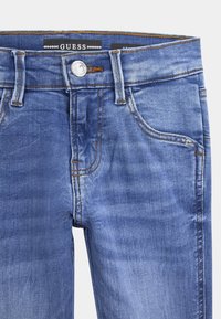 Džínové kalhoty středně modré barvy s vybledlými oblastmi, se zapínáním na předním zipu a knoflíku, pěti kapsami a oranžovými stehy.