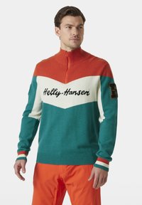Sweter z dzianiny z wysokim kołnierzem, w kolorach pomarańczowym, turkusowym i białym, z czarnym haftem logo oraz prążkowanymi mankietami.