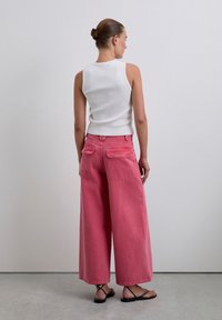 Pantaloni rosa a gamba larga in tessuto denim con tasche posteriori, abbinati a un top bianco a coste senza maniche e sandali neri piatti.
