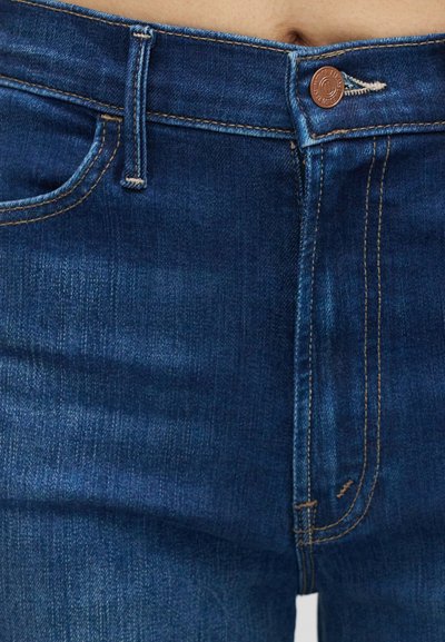 Σκούρα μπλε denim τζιν με κλασικό σχέδιο, πέντε τσέπες και αντίθετη πορτοκαλί ραφή. Διαθέτουν μεταλλικό κουμπί και φερμουάρ.