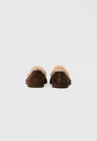 Pruunid nahast sussid, mille kaeluses on beež sünteetiline karv. Madal profiil koos lapiku, tekstuuriga tallaga. Lihtne ja funktsionaalne stiil.