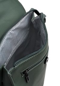 Zelený batoh z umělé kůže s hlavním přihrádkou na zip, s šedou podšívkou s chevronovým vzorem a vnější kapsou na zip.
