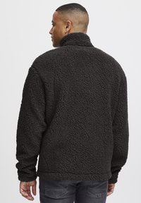 Pullover in pile nero con colletto alto, superficie testurizzata e maniche lunghe. Presenta una vestibilità comoda e dettagli nelle cuciture laterali.
