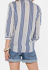 Gestreifte Bluse aus leichtem Stoff; mit blau-weißen vertikalen Streifen, Dreiviertelärmeln und Knopfdetail an den Manschetten.