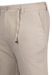 Beige Leinenhose mit strukturiertem Obermaterial, elastischem Bund, Kordelzugverschluss und zwei seitlichen Taschen. Knopfdetails am Bund.