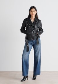 Mustast nahast mootorrattajope, millel on lukuga eesmine osa, epauletid ja kaks küljetaskut. Kombineeritud siniste laiade püksidega ja mustade kõrge kontsaga saapatega.