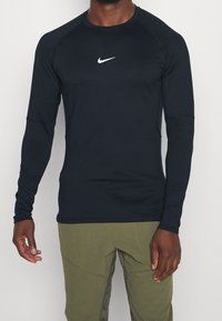 Černé sportovní tričko s dlouhým rukávem, kulatým výstřihem a ribbovanými detaily, s bílým logem Nike swoosh na hrudi.