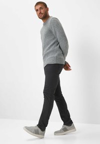Grijze gebreide trui met ribbelrand, gecombineerd met zwarte slim-fit broek en grijze sneakers met een gestructureerd patroon. Casual look.