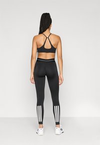 Brassière de sport noire avec un dos nageur, associée à un legging noir taille haute orné de trois bandes blanches sur chaque jambe.