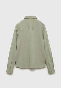 Olivgrön skjortjacka i texturerat tyg, långärmad med knäppning vid ärmsluten. Har en klassisk krage och sydd bakre ok.