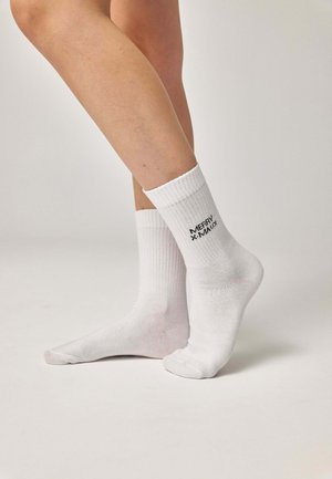Calzini bianchi di cotone con polsini a coste e testo nero con la scritta "MERRY MAUM" sul lato, indossati su piedi nudi contro uno sfondo chiaro.