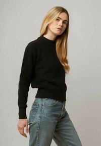 Schwarzer, gerippter Strickpullover mit hohem Kragen und enganliegenden Bündchen, kombiniert mit hellblauen Jeans, die einen lässigen Schnitt und eine angenehme Textur aufweisen.