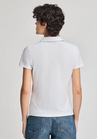 Polo shirt blanc avec un col, des manches courtes et une coupe ajustée, associé à un short en denim bleu taille haute. Texture de tissu lisse.