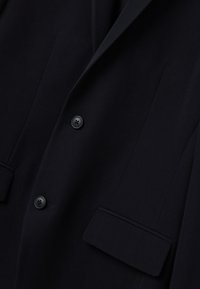 Blazer navy realizzato in tessuto liscio con due bottoni neri, rever a sottogola e una tasca sul petto con dettagli a busta.