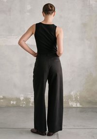 Czarny top bez rękawów zestawiony z czarnymi spodniami z szerokimi nogawkami na wysokim stanie. Prosty design, gładka faktura, minimalistyczny styl, brązowe obuwie.