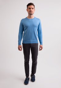 Himmelblauer Langarmpullover mit Rundhalsausschnitt, kombiniert mit dunkelgrauen Hosen und blauen Sneakers. Glatte Textur, lässige Passform.