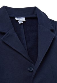 Marineblauwe colbert met een enkele knoopsluiting, gemaakt van gladde stof. De kraag en knoopdetails zijn opvallend. Label zichtbaar aan de binnenkant.