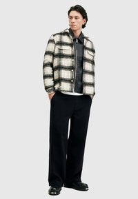 Skjortejakke i ternet uld i creme og sort, lagdelt over en sort læderjakke med lynlås, kombineret med vidde sorte bukser og sorte sko.