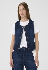 Farmer dzseki kerek nyakkivágással, gombos záródással és két elülső zsebbel. Sötétkék szín, látható varrási részletekkel.