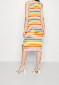 Stickad tankklänning med horisontella ränder i orange, gult, grått och ljusblått. Har sidofickor och en figursydd silhuett. Kombineras med beige klacksandaler.