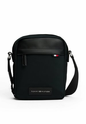 Sac bandoulière noir en nylon avec un dessus en cuir lisse, présentant un patch logo argenté et un accent tricolore sur la fermeture éclair. Sangle ajustable incluse.