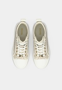 Ténis brancos com padrão texturizado bege, detalhes em metal dourado e sola de borracha branca. Apresentam biqueira redonda e design com atacadores.