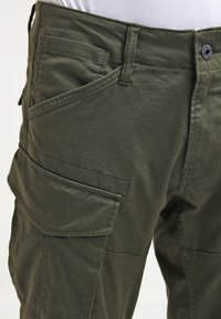 Pantalon cargo vert en tissu mélangé coton, doté d'une fermeture éclaire et d'un bouton, de multiples poches latérales, et d'une texture lisse et mate.