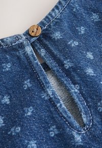Tissu en denim avec de petites impressions florales blanches, avec un bouton en bois fermant un détail d'encolure à trou de serrure.