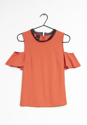 Ærmeløs koralbluse med cutouts ved skuldrene, flæsete korte ærmer og sort kravekant, hængende på en sort bøjle.