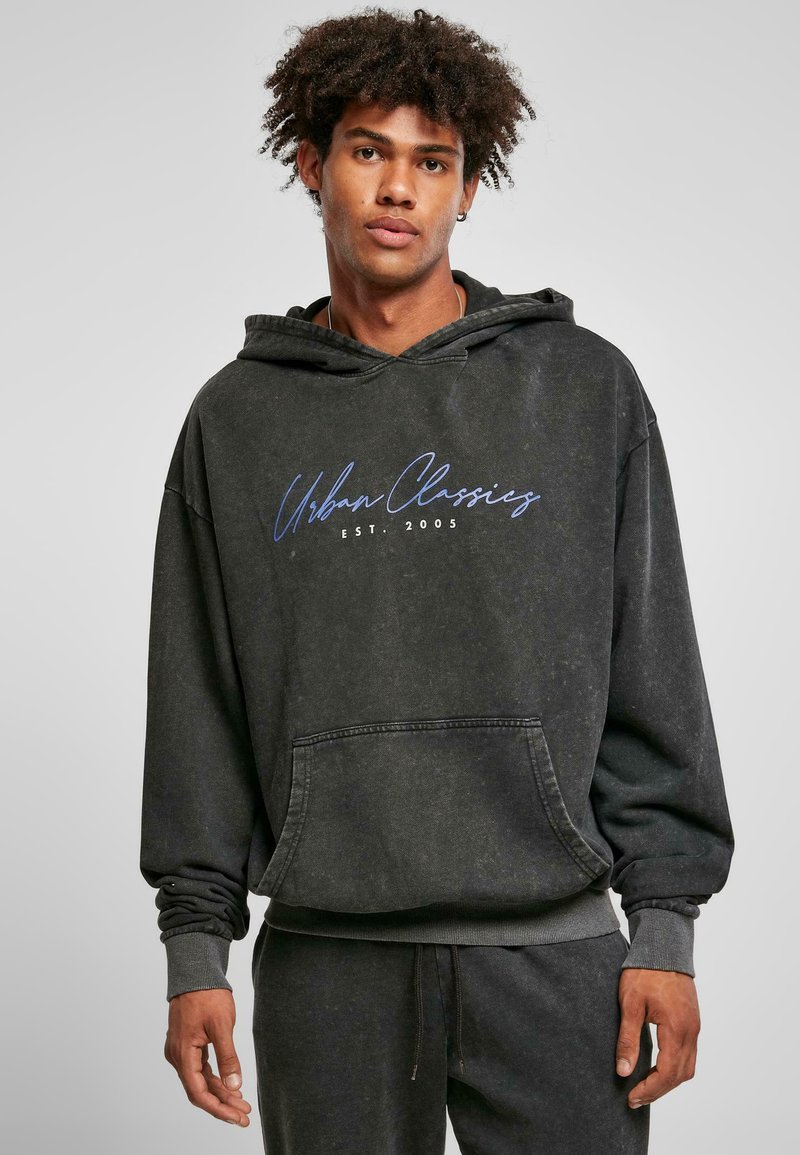 Felpa nera con cappuccio dalla vestibilità rilassata, dotata di tasca frontale e logo "Urban Classics" in scrittura blu, realizzata in un materiale morbido e texturizzato.
