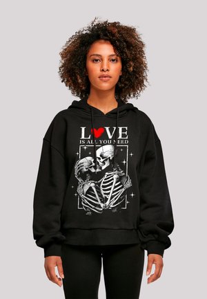 Black hooded sweatshirt featuring a skeleton graphic with the text "LOVE IS ALL YOU NEED" and a red heart detail. Relaxed fit with cuffed sleeves.
