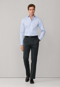 Lichtblauw button-up shirt met lange mouwen, gecombineerd met donkergroene gepofte broek en zwarte leren schoenen; gladde stoftextuur.