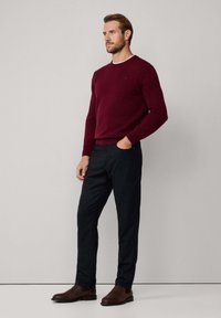 Pull en maille bordeaux avec un col rond, associé à un pantalon foncé et des bottines brunes, contrastant les textures et les couleurs.