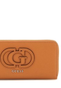Orange leather wallet with embossed logo and silver "GUESS" detail. Features a zip closure and textured finish. Rectangular shape.