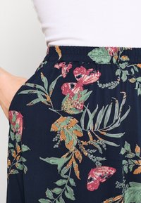 Navy fabric featuring a floral pattern with green leaves and colorful flowers and butterflies; elastic waistband; side pocket visible.