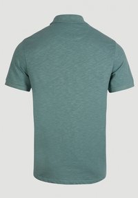 Polo shirt à manches courtes de couleur teal clair, fabriqué à partir d'un tissu texturé. Présente un col classique et un dos uni sans logos ni motifs visibles.