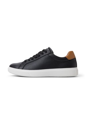 Zapatilla de cuero negro con upper texturizado, suela de goma blanca y acento en el talón marrón. Presenta cordones redondos y un diseño de puntera redondeada.