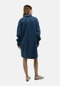 Robe chemise en denim oversize bleu foncé, dotée de longs manches, d'un col et d'un ourlet incurvé avec un détail cousu en bas.