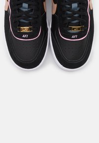 Svarta sneakers med mocka- och läderpaneler, rosa detaljer, perforerat tåparti, guldfärgad hårdvara och broderad "AF1"-logotyp på tungan.