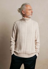 Gruby sweter typu turtleneck w sploty kablowe z prążkowanym dołem i mankietami, zestawiony z czarnymi spodniami; gładka tekstura i zrównoważony design.