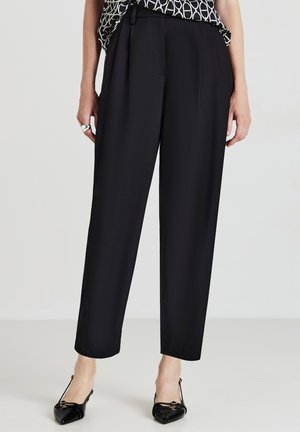 Pantalons noirs ajustés avec une coupe droite, dotés de plis sur le devant et de poches latérales. Complétés par des chaussures noires à bout pointu.