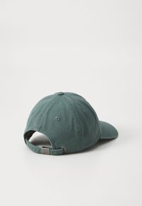 Mørkegrønn bomull baseballcap med buet skjerm, justerbar stropp og synlige sømmer. Baksiden har en klassisk lukking og ventilasjonsåpninger.
