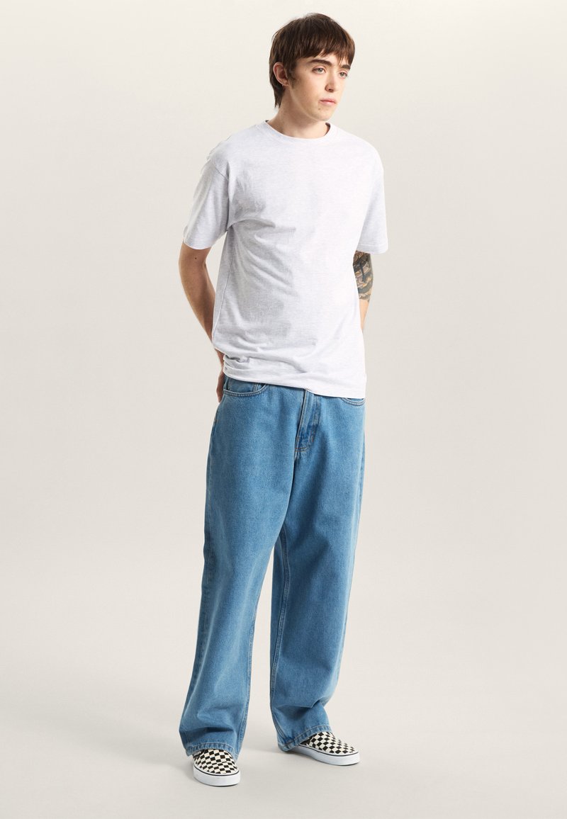 Ljusgrå kortärmad t-shirt med avslappnad passform, kombinerad med löst sittande blå denimjeans. Svartvita rutiga slip-on-skor. Minimalistisk design.