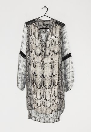 Blusa lunga e morbida con una stampa a serpente in nero e beige. Presenta una scollatura con lacci, maniche lunghe e dettagli testurizzati neri.