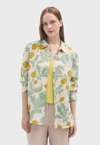 Camicia leggera e a fantasia color crema con motivi di verdure gialle e verdi. Presenta un colletto e una chiusura con bottoni, maniche arrotolate e una vestibilità comoda.